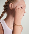 A woman with braided hair wearing the Heart Station Bracelet, a delicate gold accessory featuring multiple small heart charms.